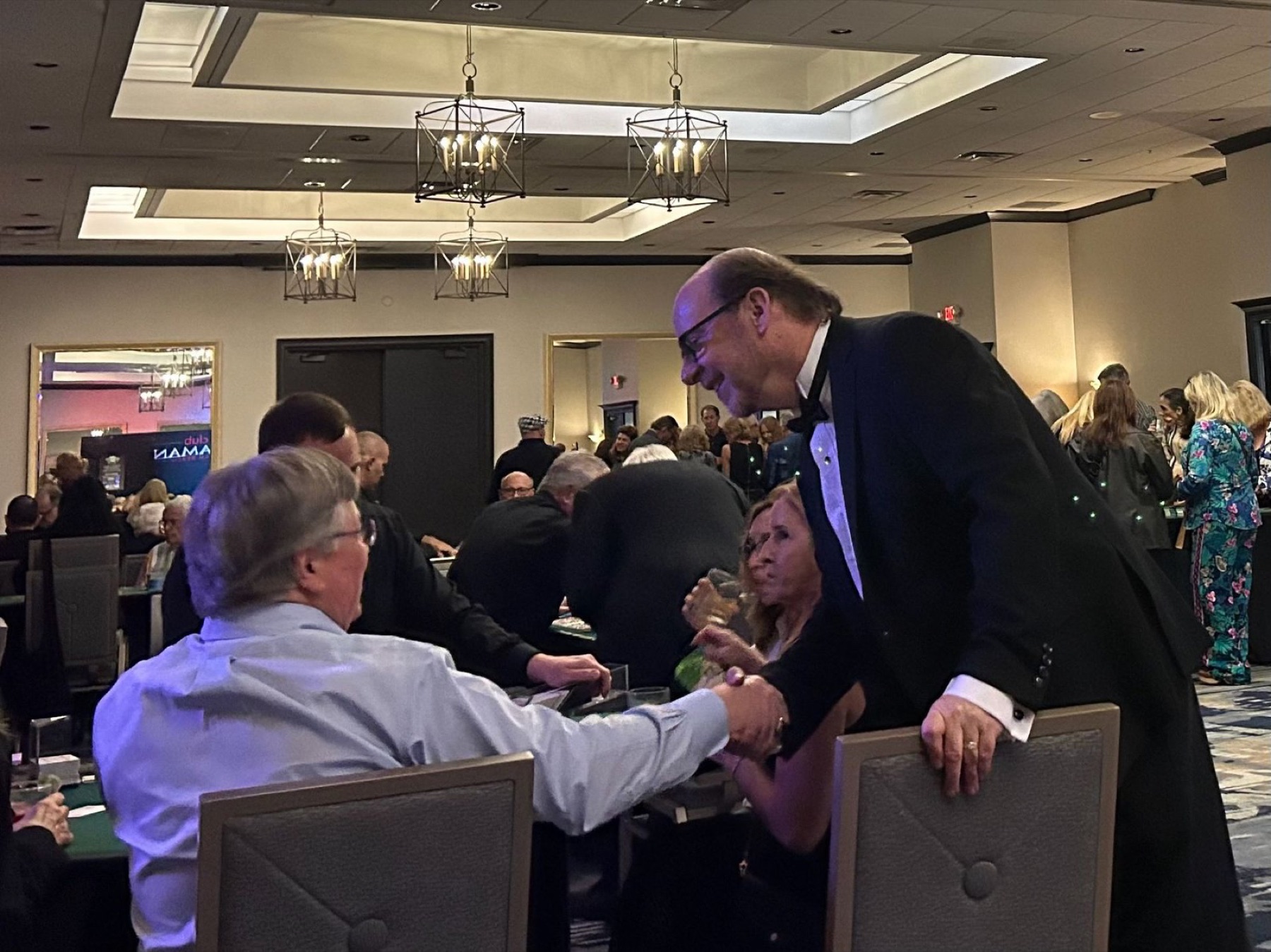 Event host greeting guests seated at a casino table during a gala